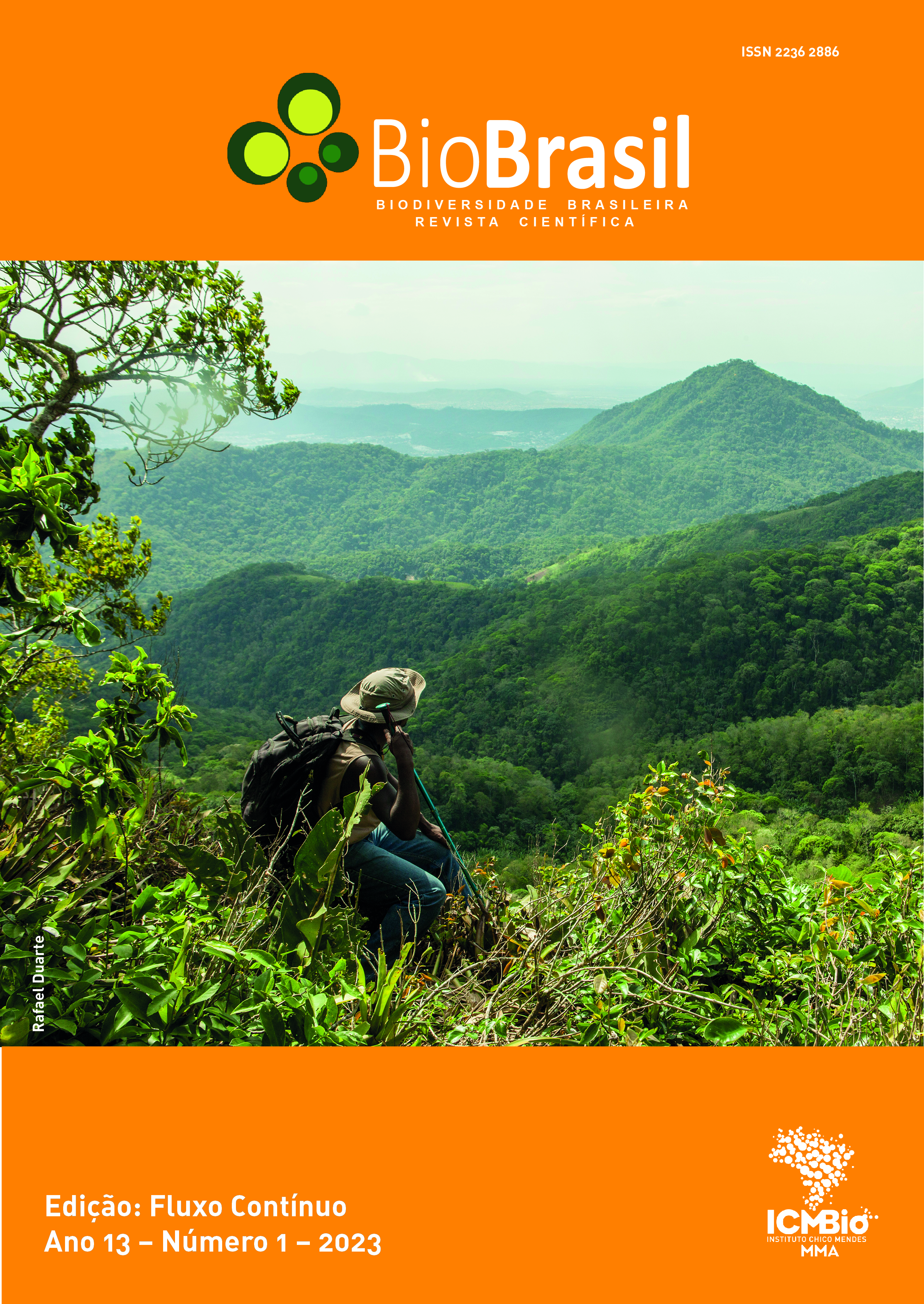 #paratodosverem: A capa da revista tem a cor laranja na parte superior e na inferior. Na parte superior, traz a logomarca da revista BioBrasil. No meio da capa, há uma foto de paisagem com montanhas, onde, sentado em um morro, um homem descansa e aprecia as montanhas ao seu redor. Ele veste calça jeans, colete bege e camisa verde. Traz um chapéu em sua cabeça, também bege. Nas costas, uma mochila grande e na mão direita um bastão de caminhada. O céu está ensolarado e enevoado. A foto é de autoria de Rafael Duarte. Na parte de baixo da capa, à esquerda, está o título da edição (Fluxo Contínuo), seguido das informações: Ano 13, Número 1, 2023. Do lado oposto, à direita da página está a logomarca do Instituto Chico Mendes de Conservação da Biodiversidade (ICMBio).